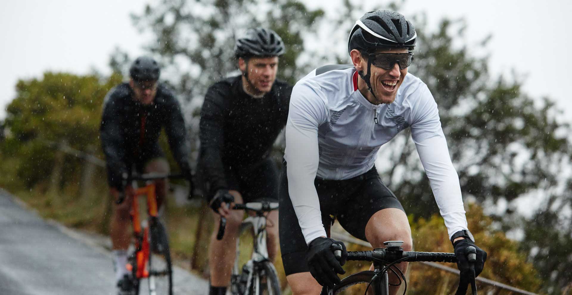 Drei Rennradfahrer fahren hintereinander im Regen über eine Straße.